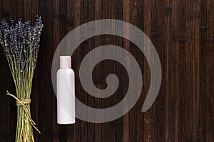 Ecological cosmetics. An empty pink bottle with a cosmetic product and a bouquet of lavender on a dark wooden table. The concept