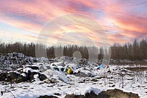 Ecological crisis. Different garbage and trash on snow at beautiful winter forest at colorful sky. Environmental pollution by