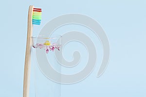 An ecological, wooden toothbrush, a glass with clean, clear water and a white daisy floating in the water on a blue background