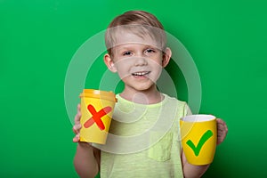 Ecology concept. Child kid boy with reusable mug and disposable paper cup, studio shoot on green background