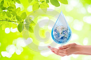 Ecology Concept : Woman hand holding planet earth globe in water drop with green natural in background.