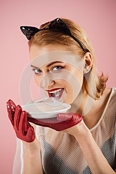 Ecology product and heath. Girl in kitten ears and red gloves with yoghurt on pink background. Cat woman eat sour cream