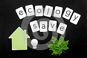 Ecology save copy with green maple leaves, house figure and lamp for eco concept on black background top view