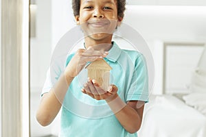 Ecology wooden house in hands of smiling African American kid
