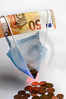 The economic effect of the pandemic - A 50 euro banknote holds up a protective mask filled with euro cents, concept