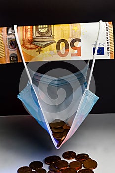 The economic effect of the pandemic - A 50 euro banknote holds up a protective mask filled with euro cents, concept