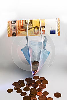 The economic effect of the pandemic - A 50 euro banknote holds up a protective mask filled with euro cents, concept