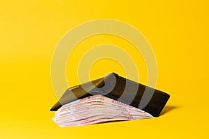 Economic prosperity. A black leather wallet lies open, filled with a stack of five-thousand-ruble bills. Yellow background. Copy