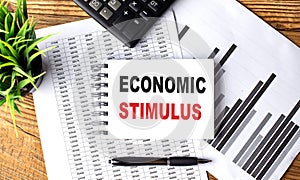 ECONOMIC STIMULUS text on notebook on chart with calculator and pen