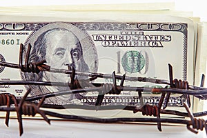 Economic warfare, sanctions and embargo busting concept. Close up US Dollar banknotes wrapped in barbed wire photo