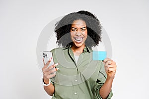 An ecstatic African-American woman celebrates with her smartphone and a credit card in hand