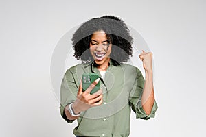 An ecstatic African-American woman celebrates while looking at her smartphone