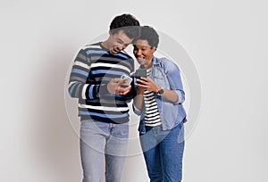 Ecstatic boyfriend and girlfriend showing mobile apps to each other and laughing on white background