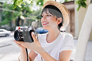 Ecstatic brunette girl with professional camera looking away smiling, enjoying amazing nature view. Charming young woman