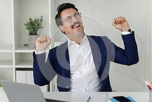 Ecstatic businessman in blue suit with eyes closed and fists pumped celebrates a victory