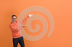 Ecstatic businessman in eyeglasses with arms raised advertising on copy space over orange background