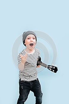 Ecstatic little boy in a cap with guitalele under arm, shouting at someone