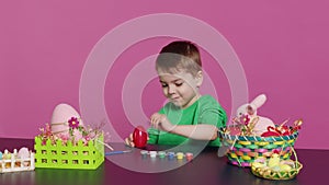 Ecstatic little kid using watercolor and paintbrushes to decorate eggs