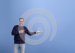 Ecstatic salesman pointing and showing empty hand while marketing new product over blue background