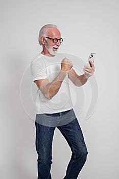 Ecstatic senior male professional reading good news on smart phone and gesturing on white background