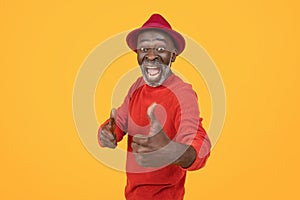 Ecstatic senior man in a red sweater and hat giving a thumbs up, his face beaming