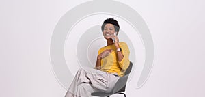 Ecstatic young businesswoman making a business call over mobile phone on chair over white background