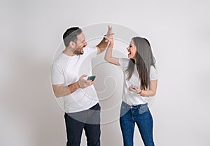 Ecstatic young couple giving high-five after reading good news over smart phones on white background