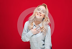 Ecstatic young woman keep hand on chest, isolated on red background. Pleased cute girl