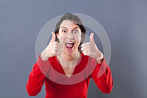 Ecstatic young woman shouting with thumbs up for excitement photo