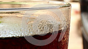 ECU of the top of a glass of cola-colored fizzy drink with indistinct backgro