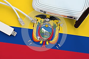Ecuador flag depicted on table with internet rj45 cable, wireless usb wifi adapter and router. Internet connection concept
