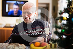 Ederly man sitting at home table with tablet during New Year celebration