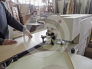 Edge banding machine. Coils of furniture finishing edges plastic band for banding machines. A worker pastes an edge on the machine