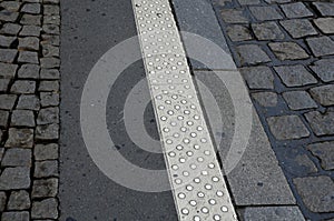 On the edge of the sidewalk is a white safety line with bumps protrusions that warn blind people that they are approaching the tra