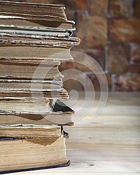 The edge of a stack of old books recumbent on a wooden table. Close-up