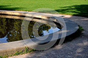 Edge of a stone sandstone circular fountain in the park. built of sandstone filled with water. lined with a light threshing gravel