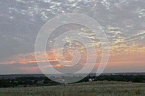 The edge of the village with small houses under a light blue sky. During a light pink sunset