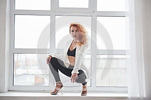 Edge of the windowsill. Attractive redhead woman posing in the spacey room near the window