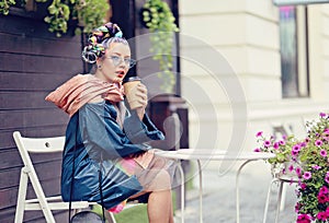 Edgy girl with extravagant look sitting at a coffee shop table. Crazy appearance on the boulevard in old town - Avant-garde