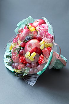 Edible bouquet of fruits and flowers on a gray background, vertical