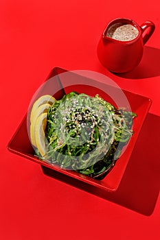 Edible Green Algae salad with nut sauce in red color boul at red background with sunlight and shadows, minimalism