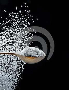 Edible salt crystals falling down into the wooden spoon at black background