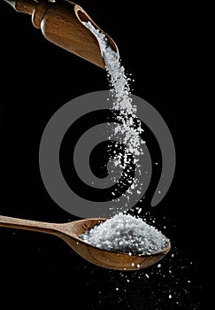 Edible salt crystals falling down into the wooden spoon at black background