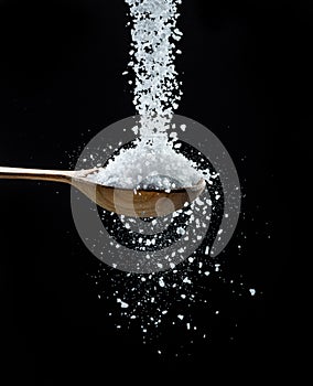 Edible salt crystals falling down into the wooden spoon at black background