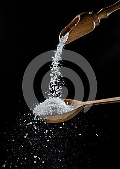 Edible salt crystals falling down into the wooden spoon at black background