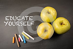 Educate Yourself Concept. Text, apples and colored pieces of chalk on a dark blackboard