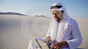 Educated male Muslim Arabian UAE Sheikh architect sits with gadg