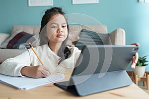 Education. Asian little girl is learning with online tutor via the internet on tablet digital at home morning. Asia children watch