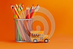 Education and back to school concept. Yellow retro school bus and pencils in basket on orange background.