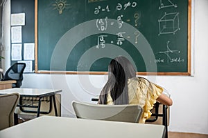 Back view of school girl on lesson in classroom write hardworking on blackboard